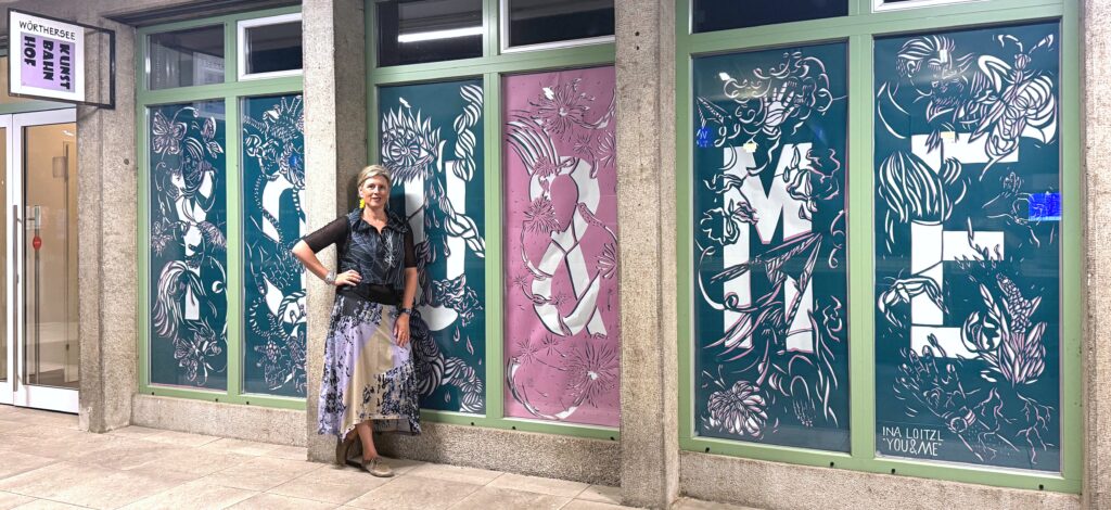 Ina Loitzl vor ihrer Fensterinstallation „You & Me“, 2026, Buchbinderpapier, Cut-out in jeweils drei Schichten, sechsteilig, je 187 × 72 cm, Kunstbahnhof Wörthersee, Foto: Barbara Ambrusch-Rapp